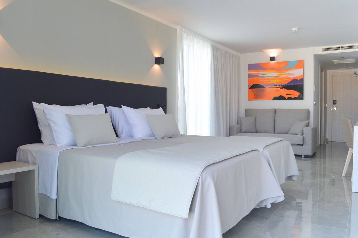 Una habitación de hotel moderna con una cama grande, un sofá, un escritorio y un cuadro en la pared.