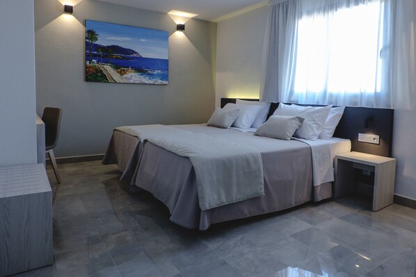 Une chambre d’hôtel moderne, dotée d’un grand lit, d’un bureau, d’une chaise et d’un tableau représentant une scène de plage.