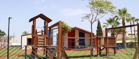 A playground with a wooden climbing structure, a swing set, and a fenced area.