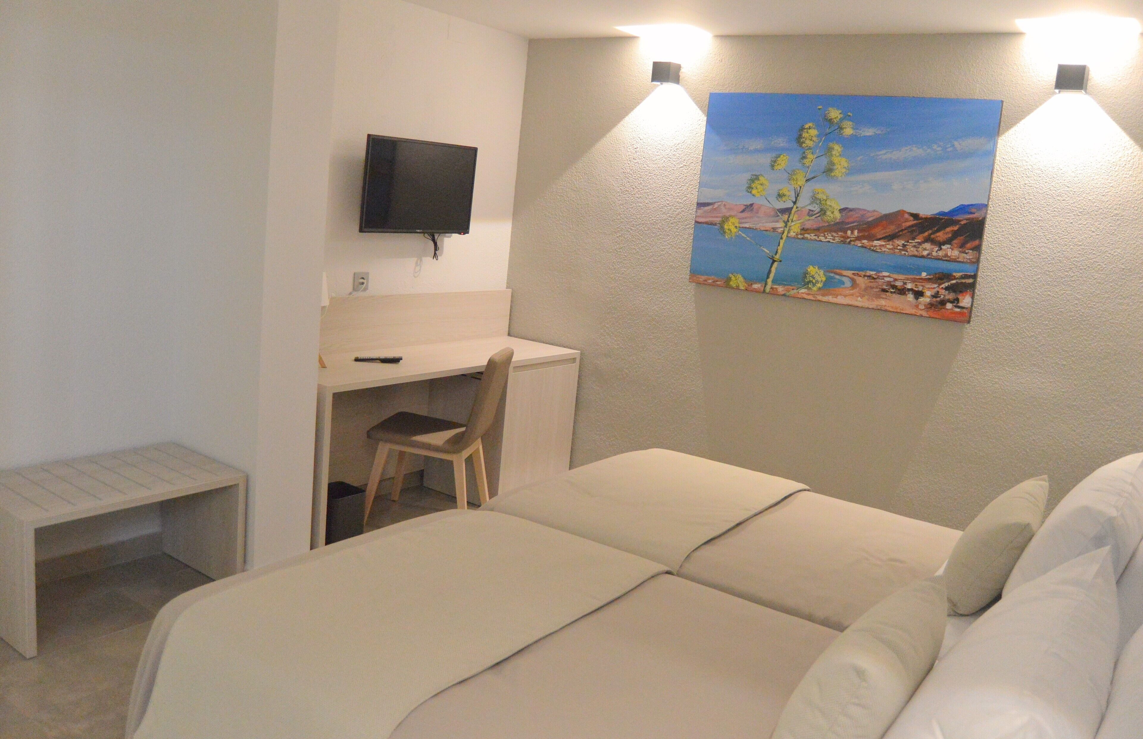 Une chambre à coucher avec un lit, un bureau, une chaise, un téléviseur et un tableau accroché au mur.