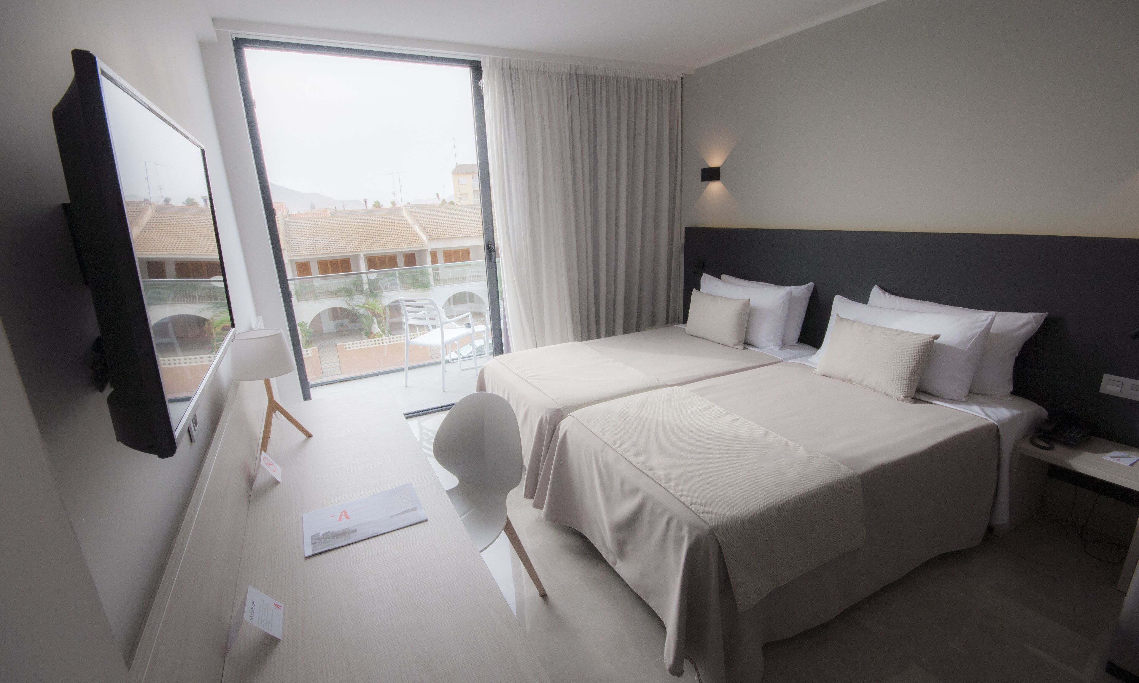 Habitación de hotel con una cama grande, un escritorio, una silla y un televisor. Cuenta con un balcón y vistas a edificios.