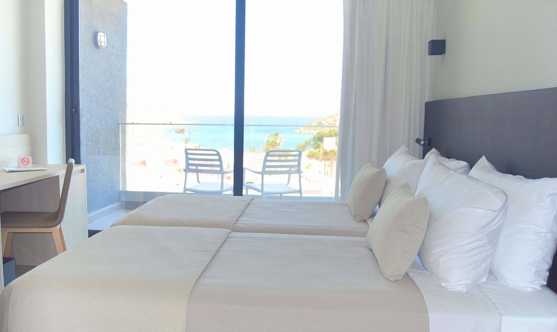 Habitación de hotel con dos camas, un escritorio y vista a la playa.