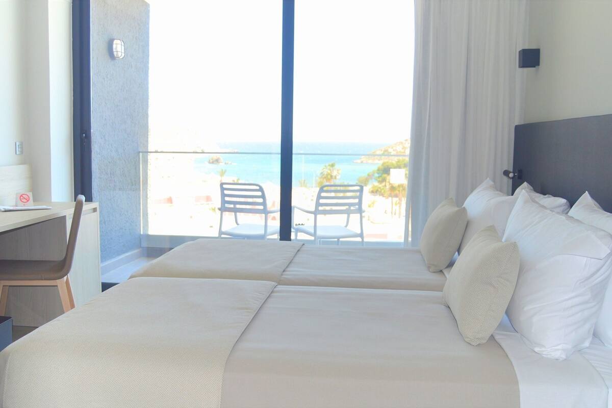 Habitación de hotel con dos camas, un escritorio y vista a la playa.