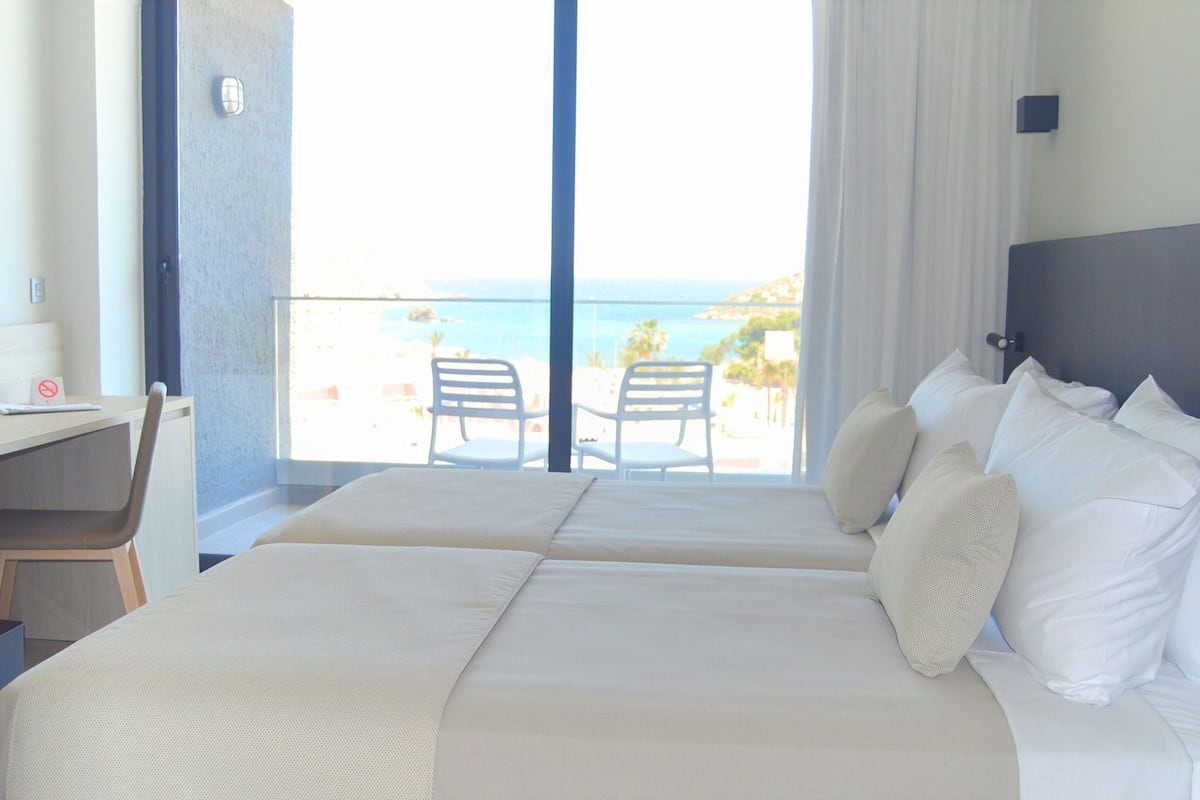 Habitación de hotel con dos camas, un escritorio y vista a la playa.