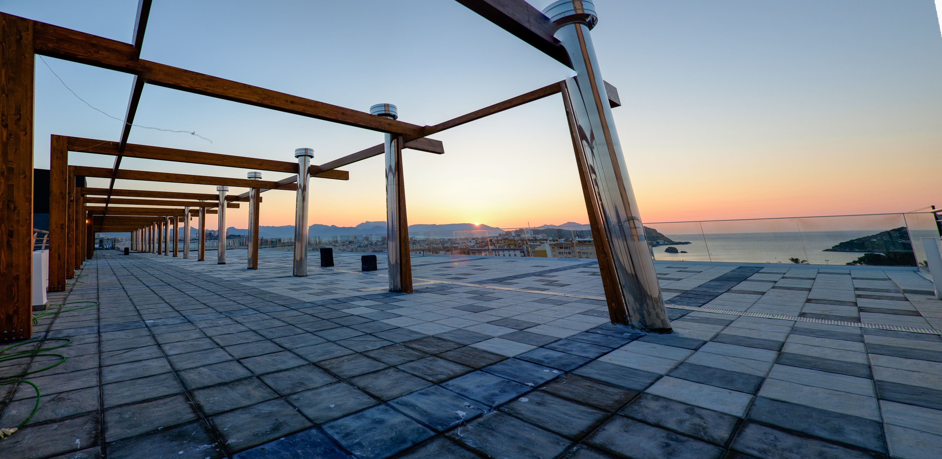 Une terrasse sur le toit offrant une vue sur le coucher de soleil sur l’eau, agrémentée d’une pergola en bois et d’un sol carrelé.