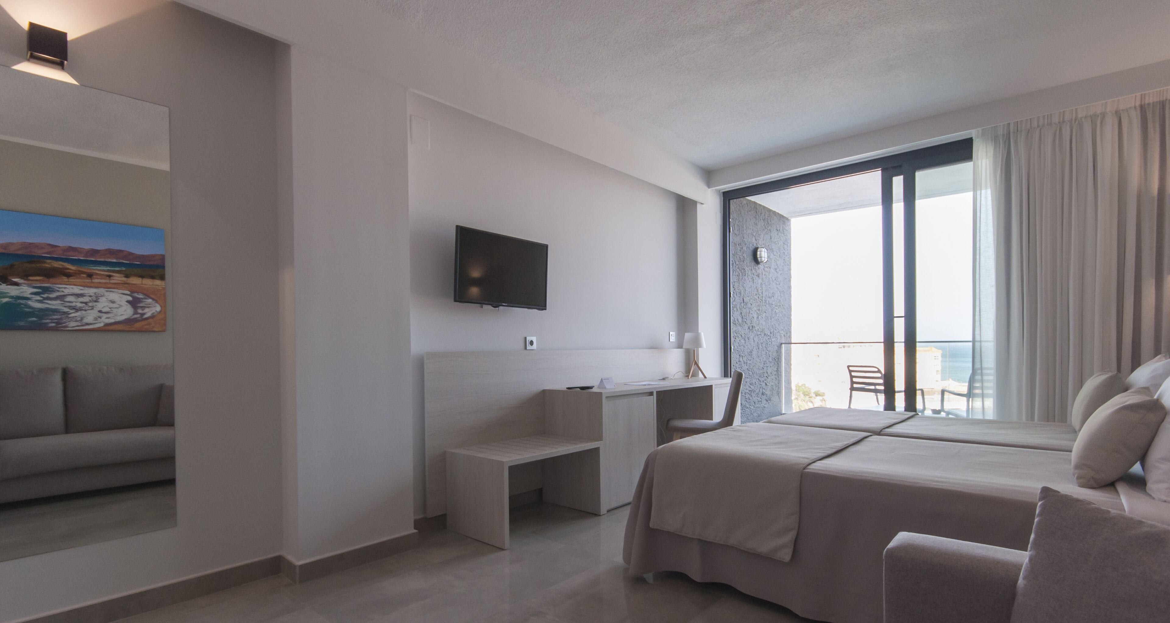 A modern hotel room with a bed, a desk, a TV, and a balcony with a view.