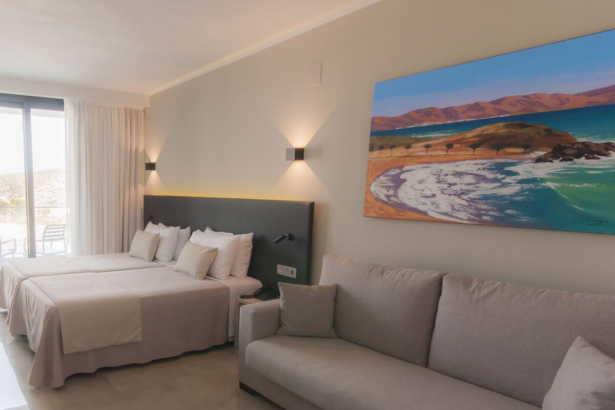 Una habitación de hotel con cama, sofá, escritorio y un cuadro de una playa.