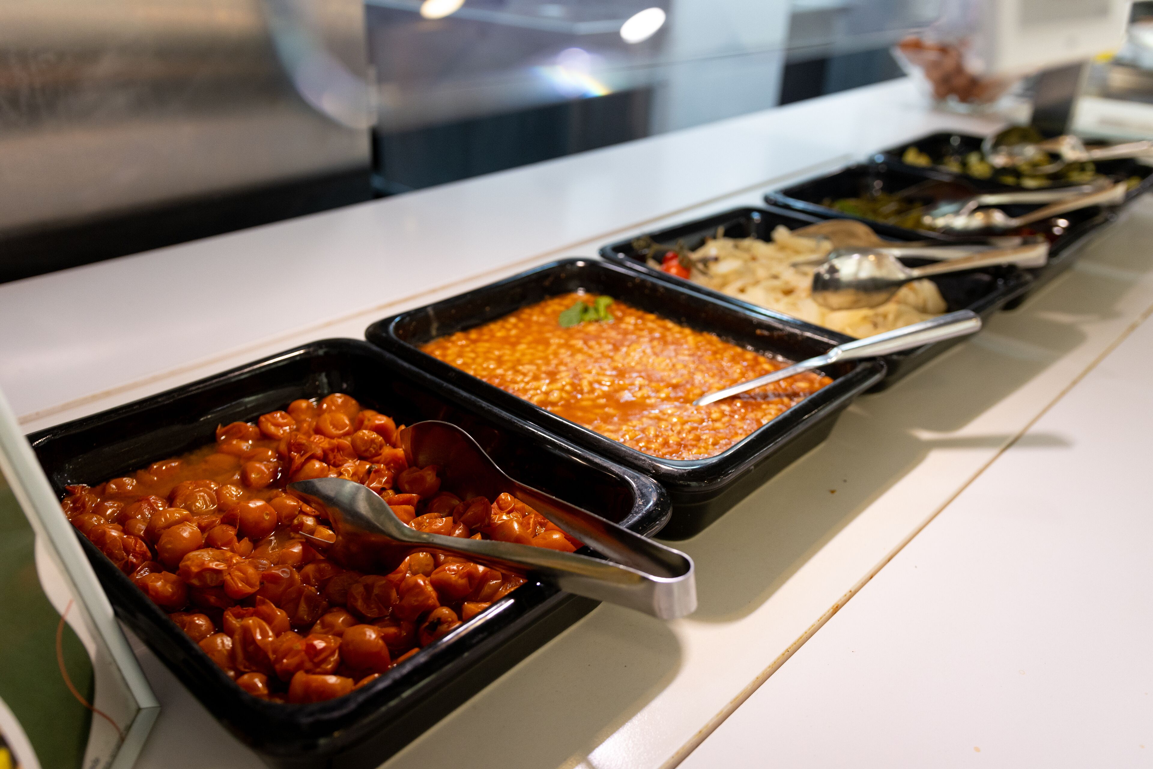 A buffet with various dishes in black trays, including a red sauce and a brown sauce.