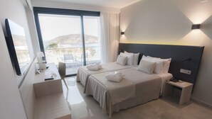 Habitación de hotel con dos camas, un escritorio, una silla y un ventanal con vistas al mar y edificios.