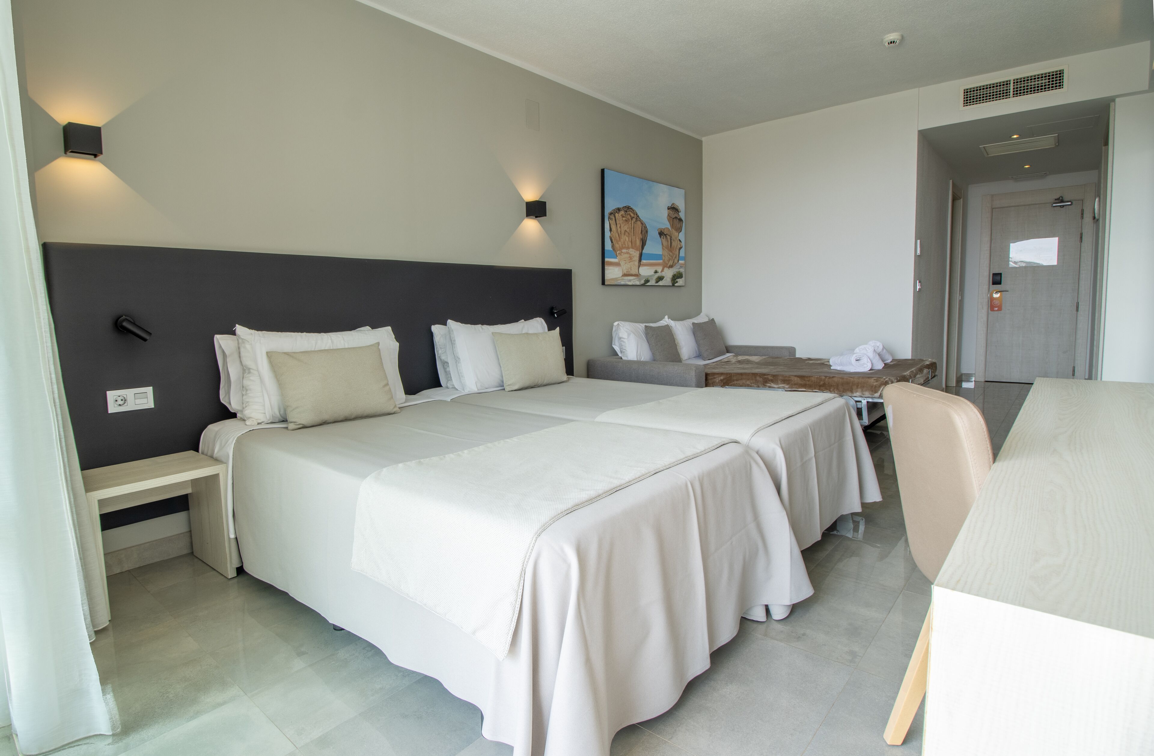 A hotel room with two beds, a desk, and a chair.