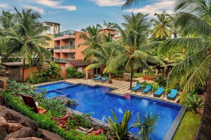 A swimming pool surrounded by palm trees and lounge chairs, with a building in the background. - Mandrem Beach Resort, a member of Radisson Individuals Retreat (Mandrem)