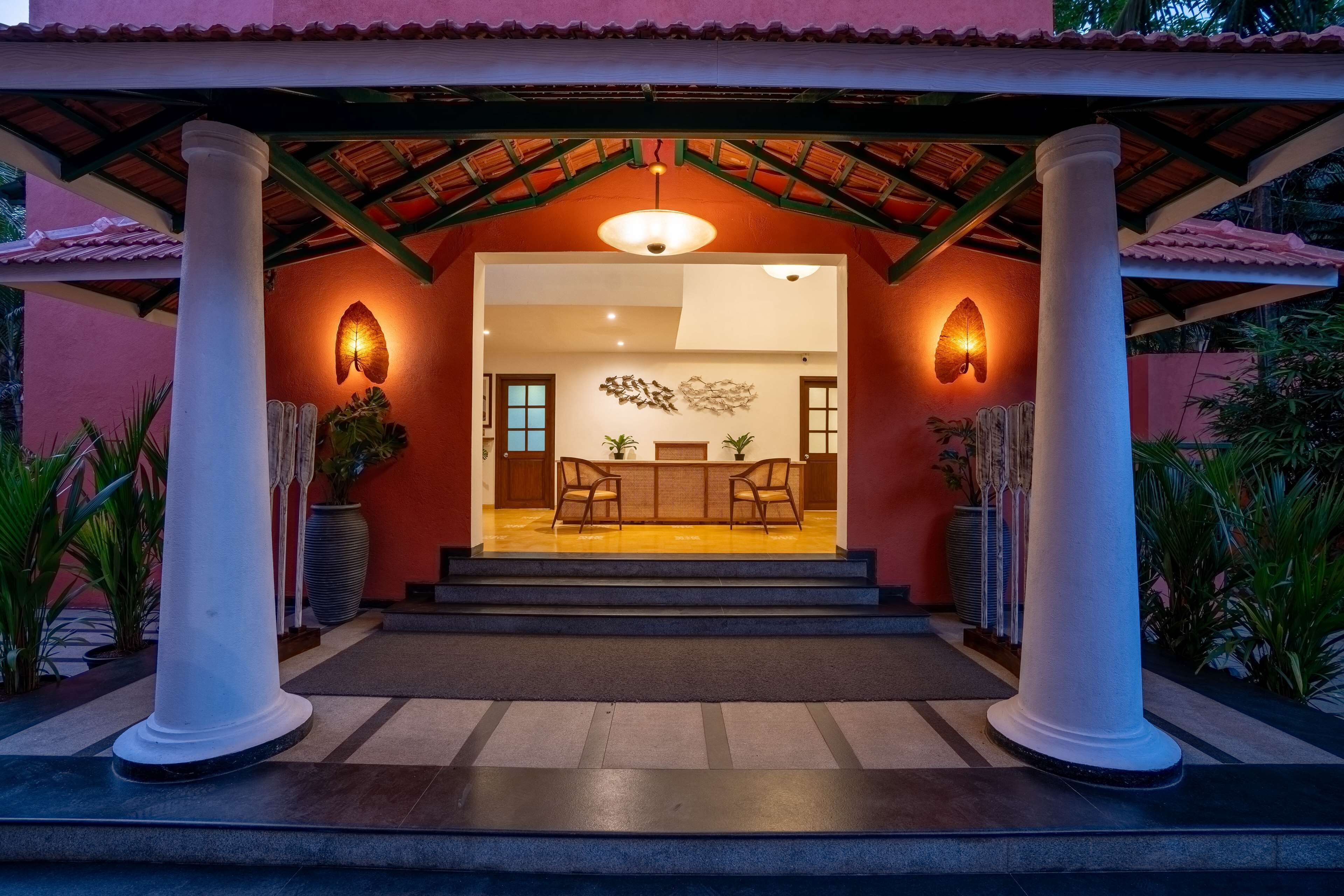 L’entrée d’un hôtel, avec un patio couvert, deux colonnes, un comptoir d’accueil et un espace salon.