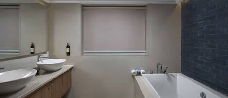 A modern bathroom with two sinks, a bathtub, and a window.