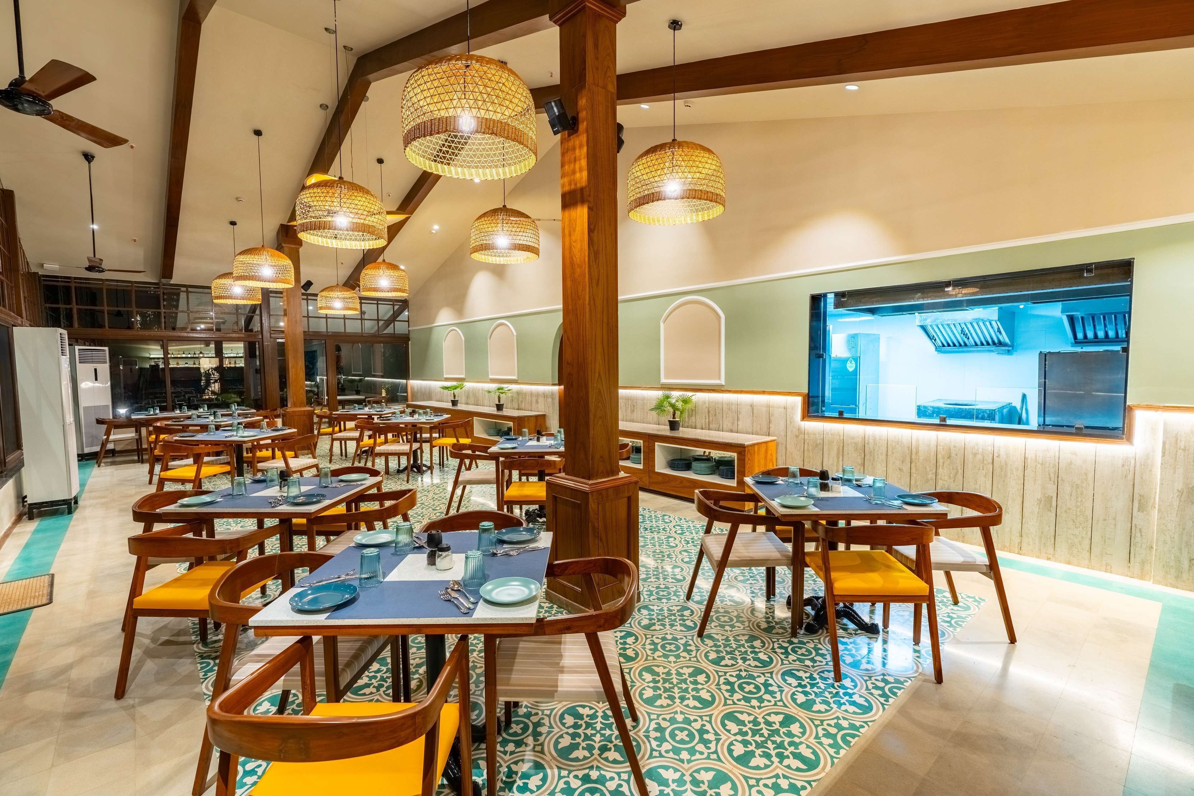 A restaurant with multiple dining tables and chairs, wooden beams, hanging wicker lamps, and a patterned floor.