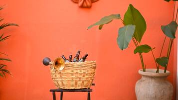 A wicker basket with bottles on a small table against an orange wall, a decorative angel, and a potted plant.