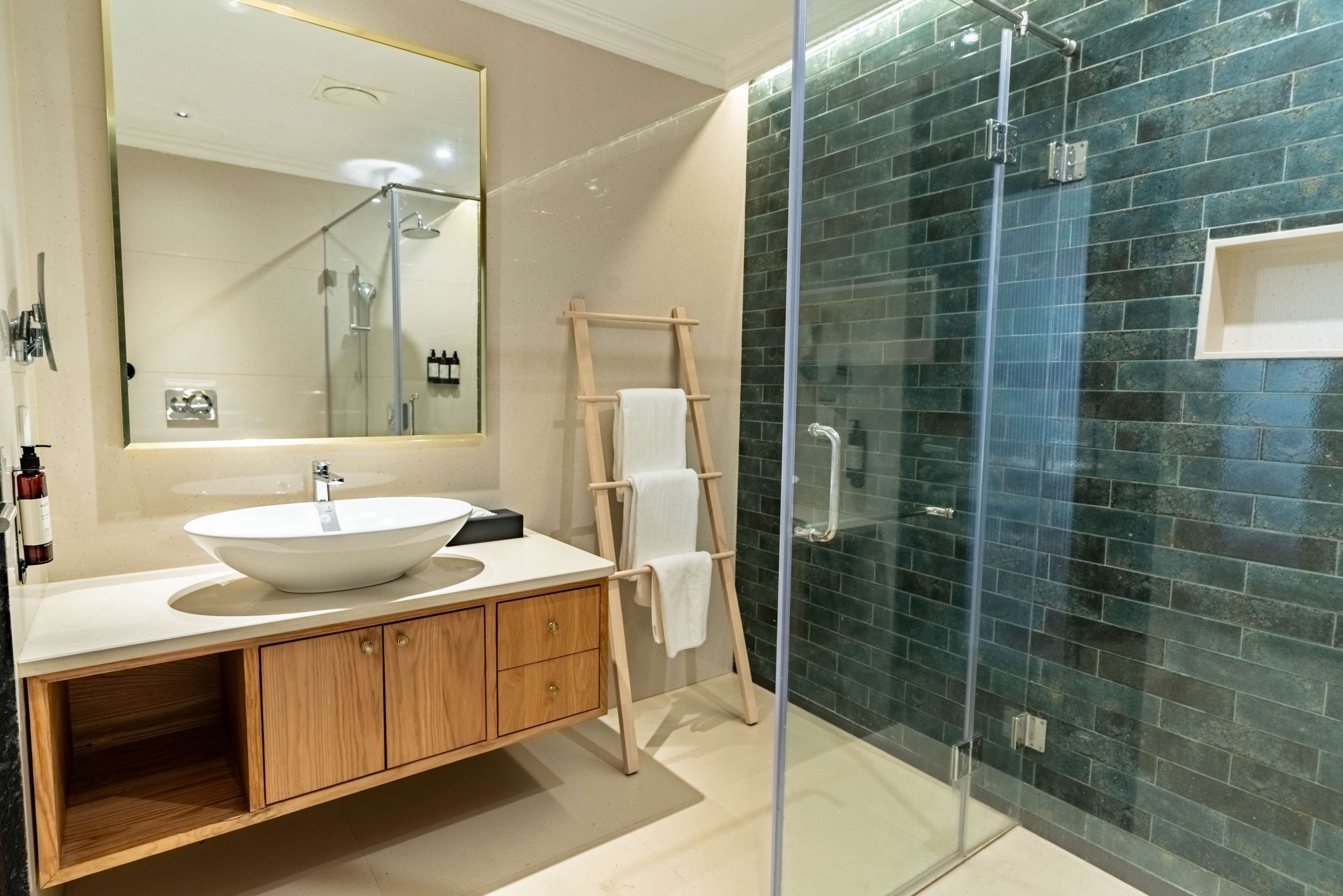 A modern bathroom with a large mirror, a wooden vanity, a glass shower enclosure, and a tiled wall.