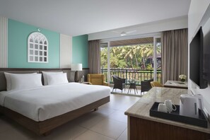 A hotel room with a large bed, a desk with a coffee maker, a TV, and a balcony with a view of palm trees. - Mandrem Beach Resort, a member of Radisson Individuals Retreat (Mandrem)