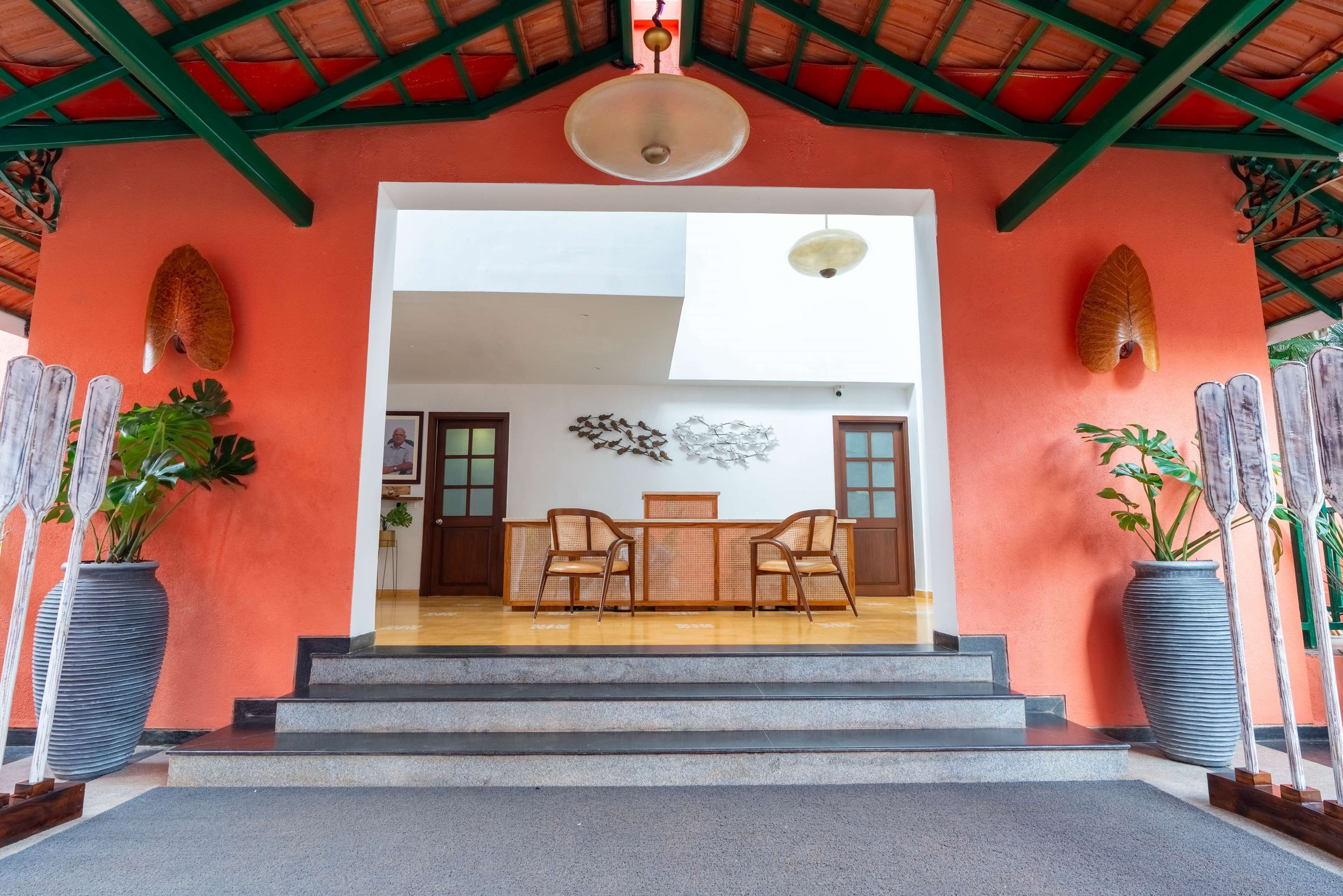 Un área de recepción con un escritorio de madera y dos sillas, una planta grande en maceta, y una escalera que conduce a un espacio interior.