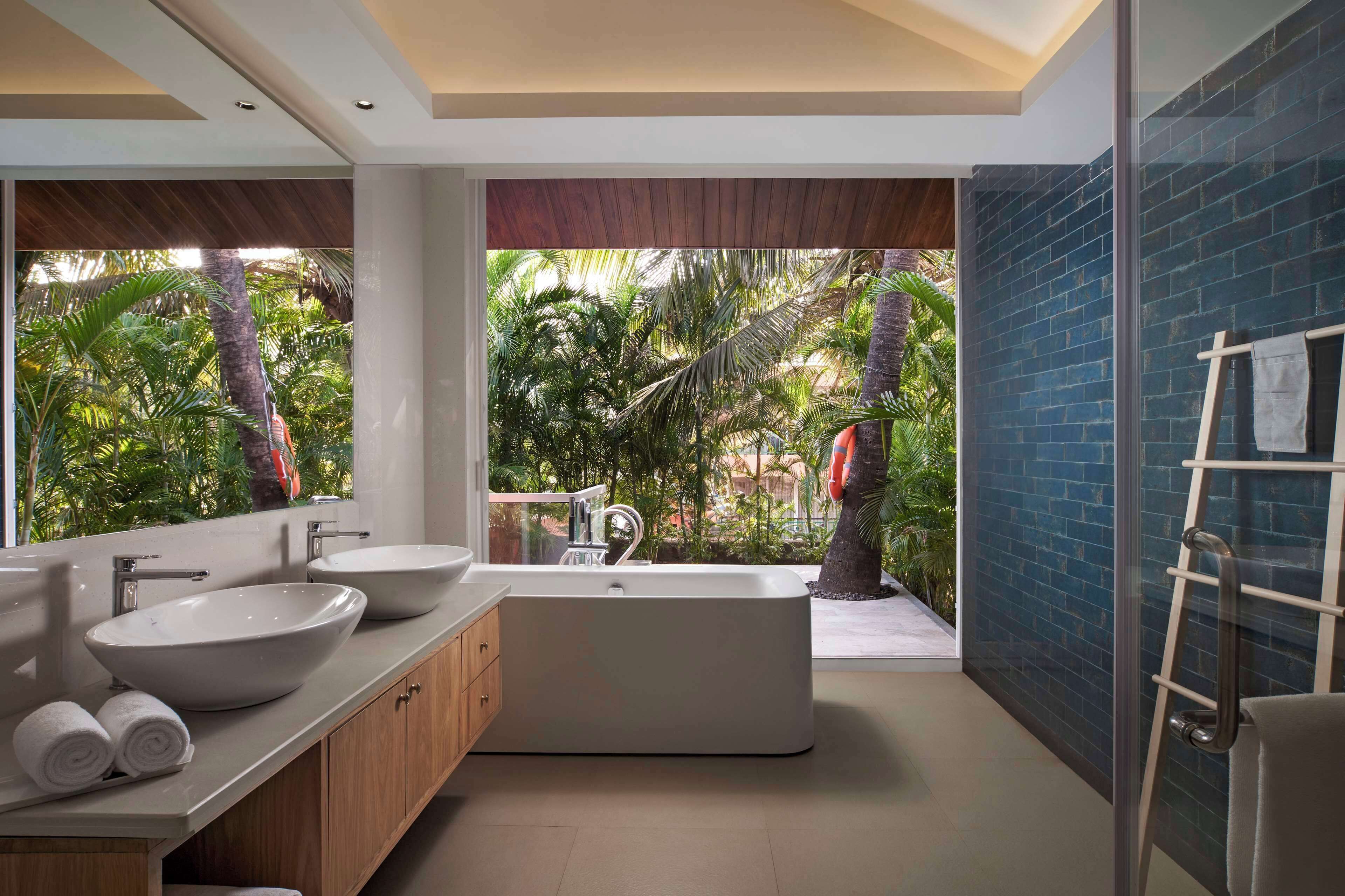 A modern bathroom with a large bathtub, two sinks, and a view of a tropical garden.
