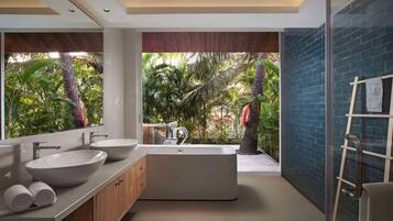 A modern bathroom with a large bathtub, two sinks, and a view of a tropical garden.