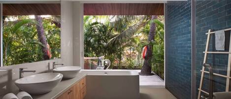 A modern bathroom with a large bathtub, two sinks, and a view of a tropical garden.