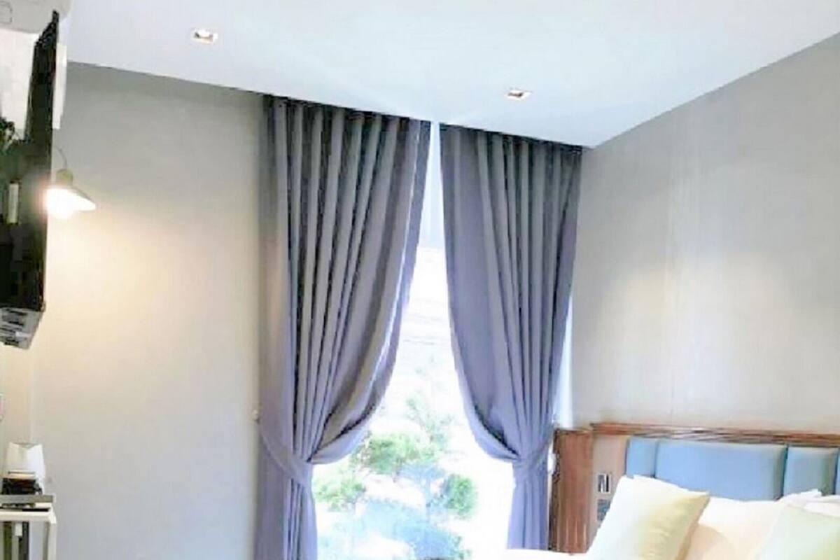 Een hotelkamer met een bed, gordijnen, een hoofdeinde en een raam met uitzicht.