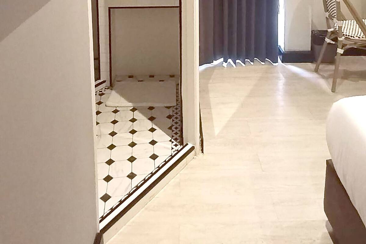 Hotelkamer met een bed, een stoel, een bureau, een spiegel en een badkamer met een wastafel en douche.