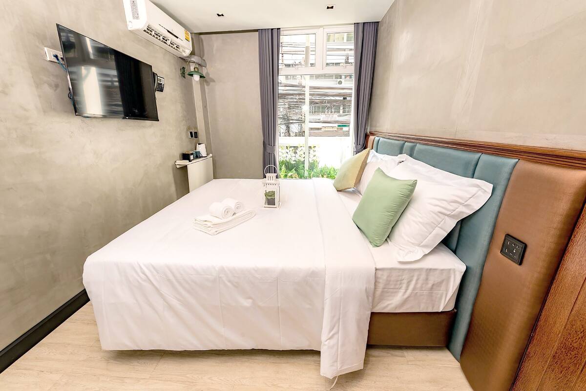 Hotelkamer met een bed, een aan de muur bevestigde televisie, een raam met gordijnen en uitzicht op buiten.