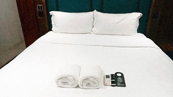Una cama bien hecha con sábanas blancas, dos toallas enrolladas, un llavero negro y un pequeño dispositivo electrónico sobre la cama.