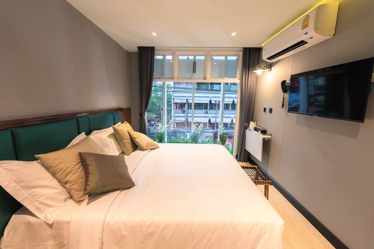 Een hotelkamer met een groot bed, een flatscreen televisie, een airconditioning en uitzicht op de stad.