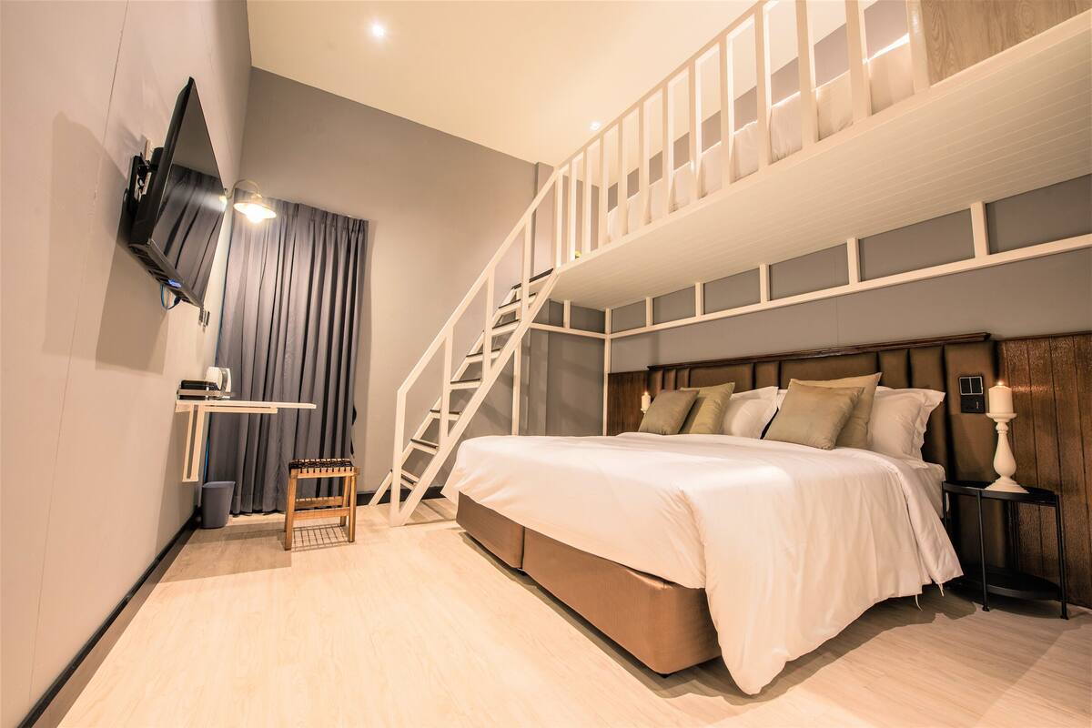 Een slaapkamer met een stapelbed, een bureau, een stoel, een aan de muur bevestigde televisie en een trap.