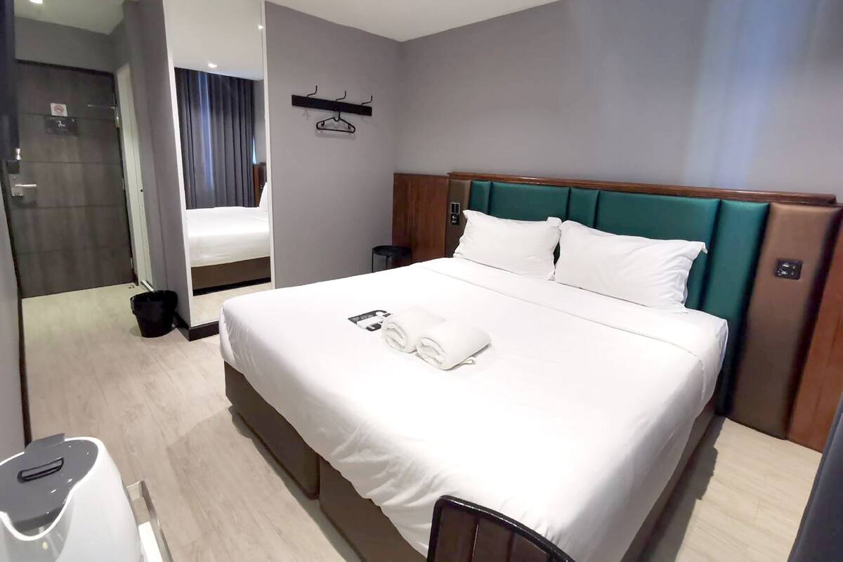 Een moderne hotelkamer met een net opgemaakt bed, een nachtkastje, een spiegel en uitzicht op de gang.