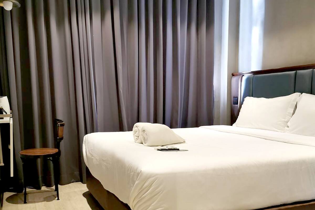 Een hotelkamer met een groot bed, een bureau met stoel en een raam met gordijnen.
