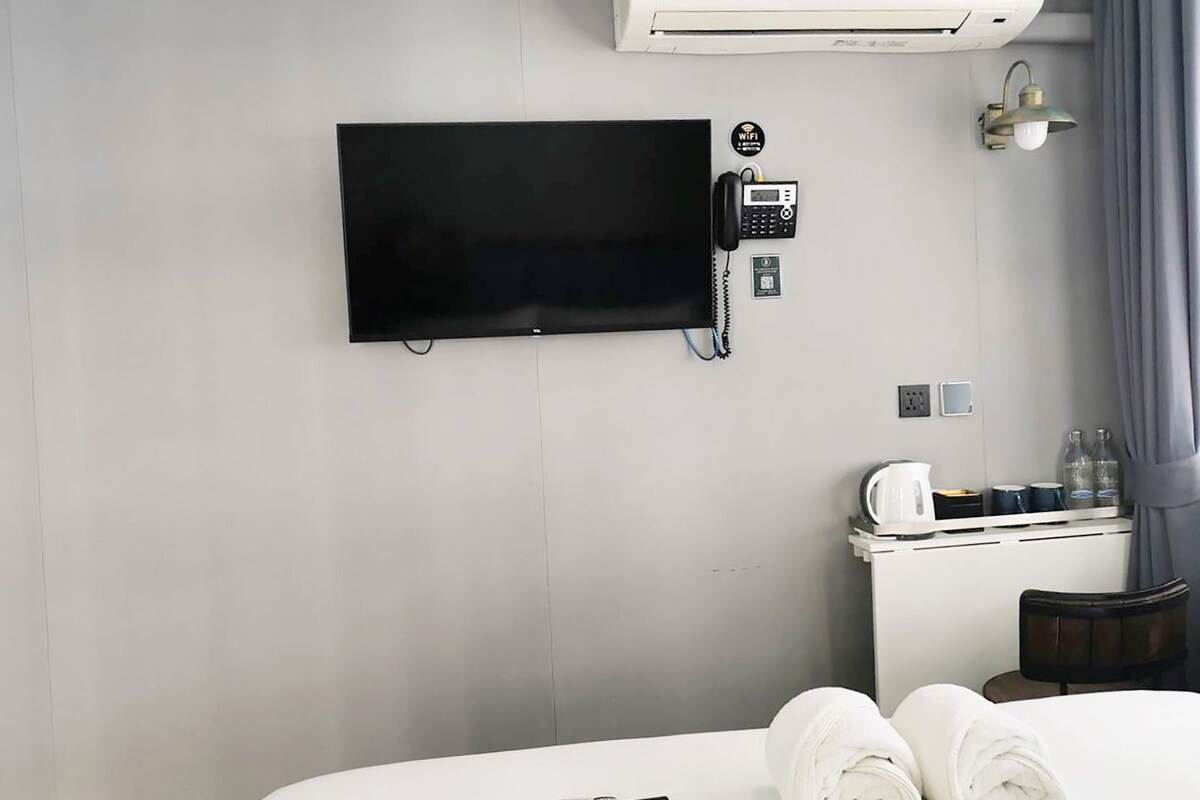 Une chambre d’hôtel équipée d’un téléviseur à écran plat fixé au mur, d’un téléphone, d’un minibar, d’un lit avec des serviettes pliées et d’une fenêtre avec des rideaux.