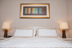 A neatly made bed with white linens and gold trim, flanked by two bedside lamps.