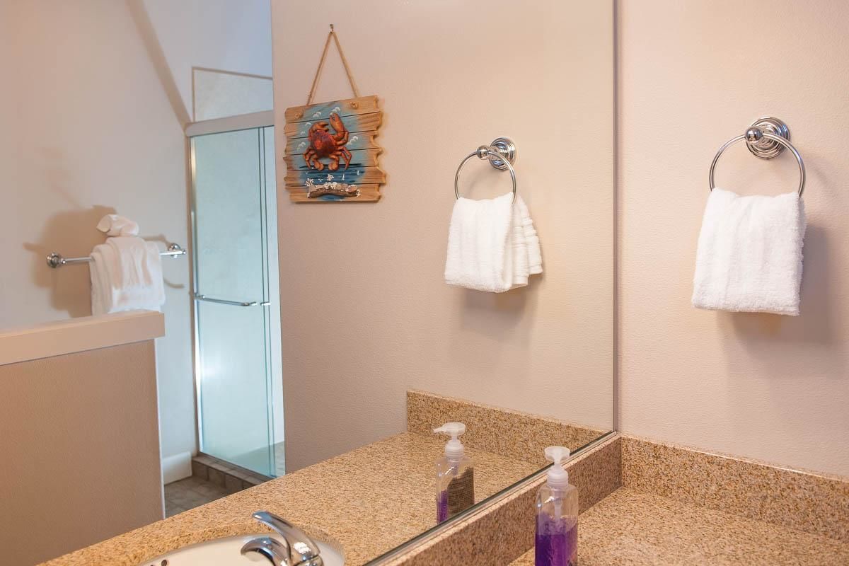A bathroom with a granite countertop, a mirror, two white towels, a wooden wall decoration, and a glass shower enclosure.