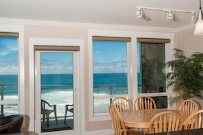 A dining area with a view of the ocean, a table with chairs, and a potted plant.