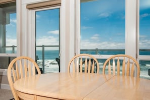 A dining area with a table and chairs, large windows with ocean views, and a view of the sea.