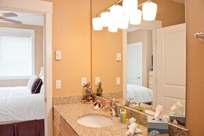 A hotel bathroom with a granite countertop sink, a large mirror, and a ceiling fan.