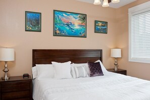 A hotel room with a large bed, two bedside tables with lamps, and three framed paintings on the wall.