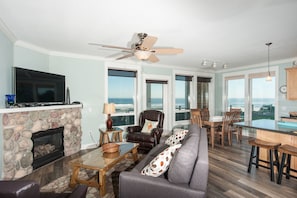A spacious living room with a stone fireplace, a leather sofa, and a dining area with a view of the ocean. - Keystone Vacation Rentals - Sand Dollar Condo (Lincoln City)