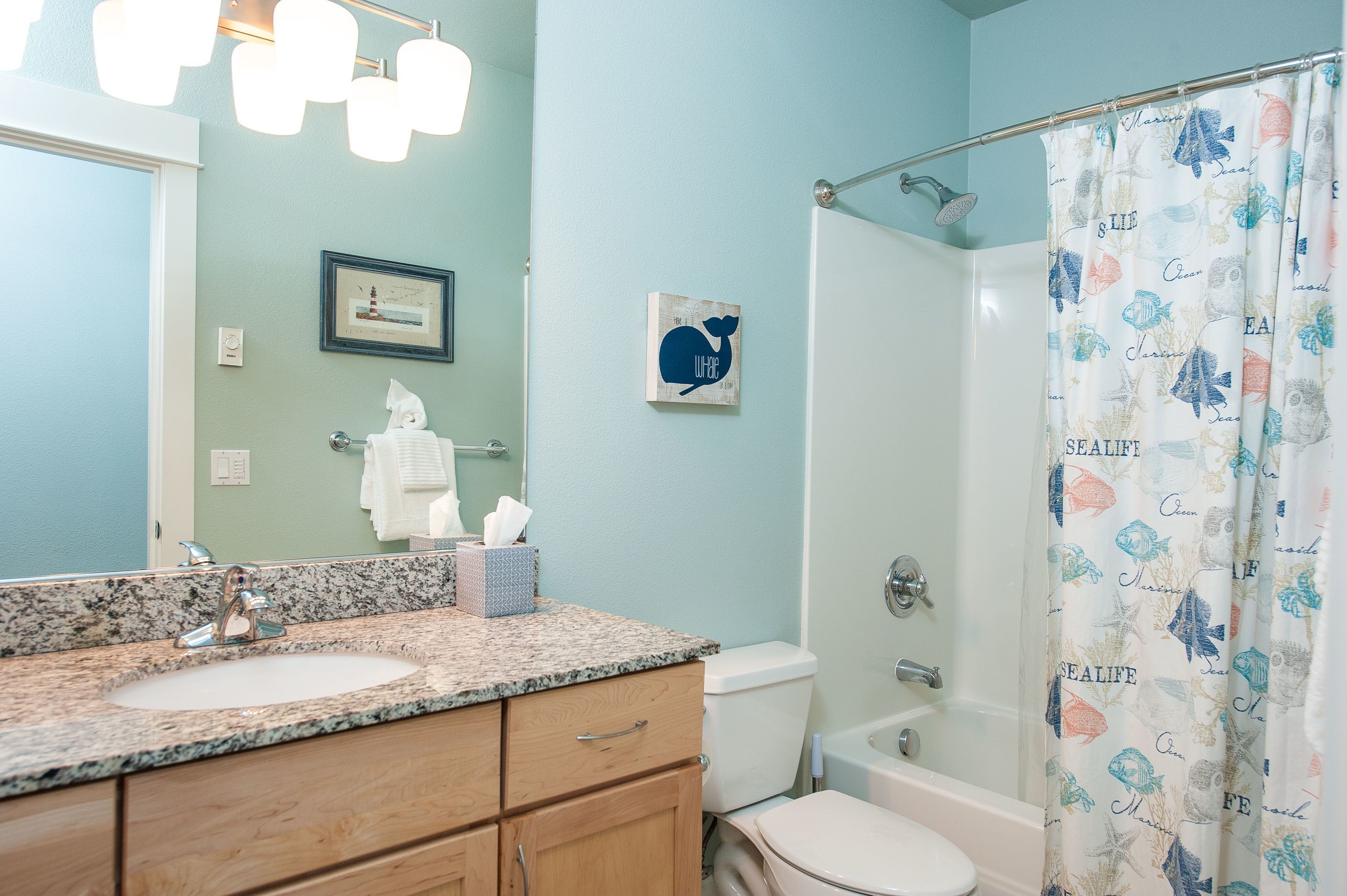 A bathroom with a granite countertop, a white sink, a toilet, and a shower curtain with a marine theme.