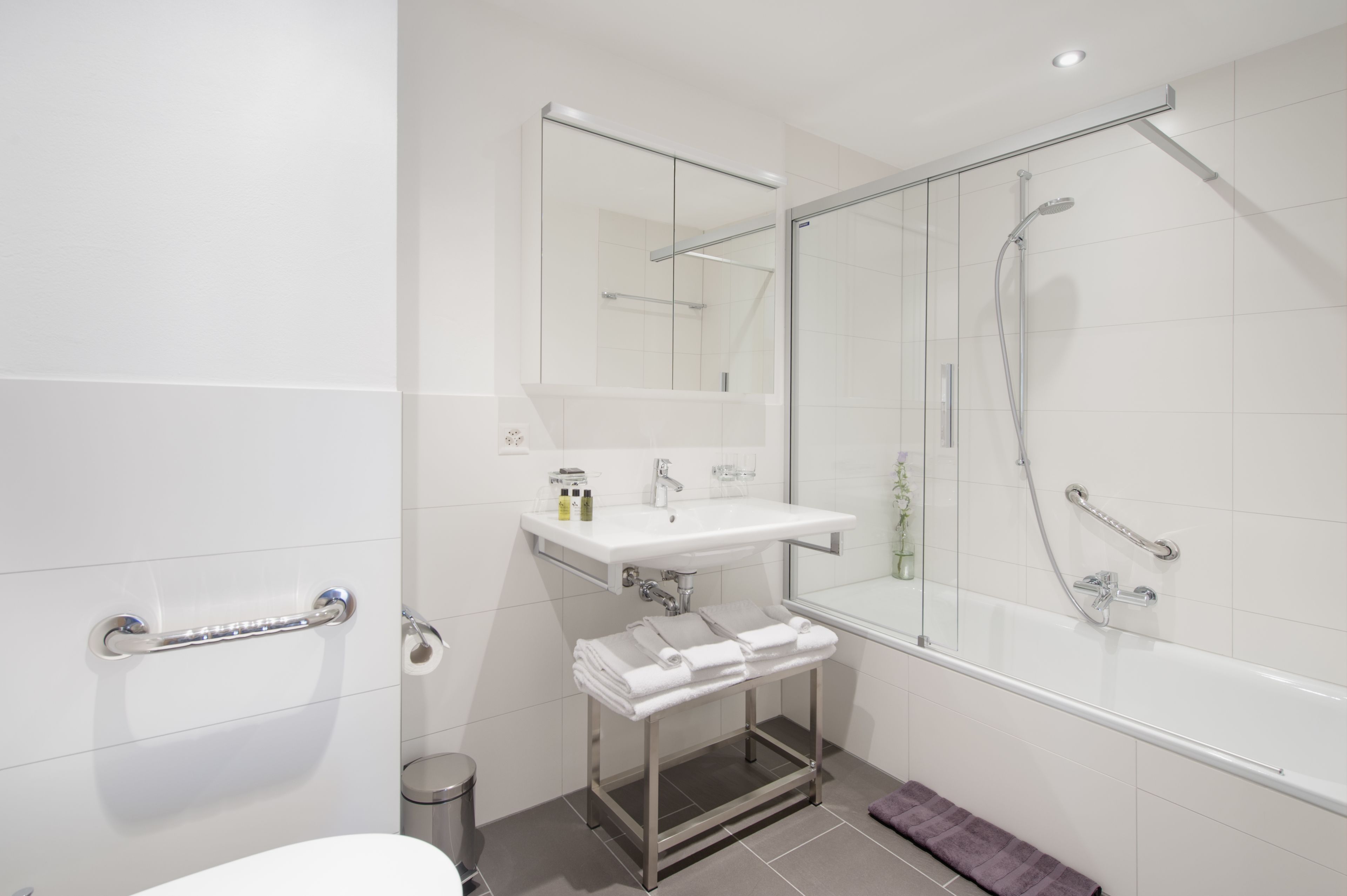A modern bathroom with a glass-enclosed shower, a white sink with a mirror above it, and a towel rack.