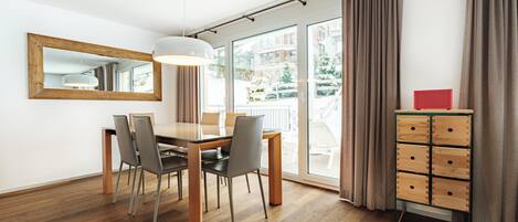 A modern dining area with a wooden table and chairs, a pendant light, a mirror, and a view of the outdoors.