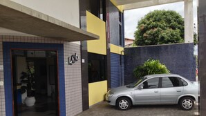 A building with a tiled facade, a car parked in front, and a potted plant near the entrance. - Hotel Kalilândia (Feira de Santana)