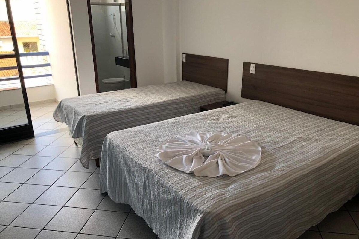 Habitación de hotel con dos camas, baño y puerta corrediza de vidrio al exterior.