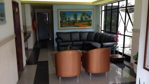 A modern lobby with a black leather sofa, two brown armchairs, a glass coffee table, and a painting of a landscape on the wall. - Hotel Kalilândia (Feira de Santana)