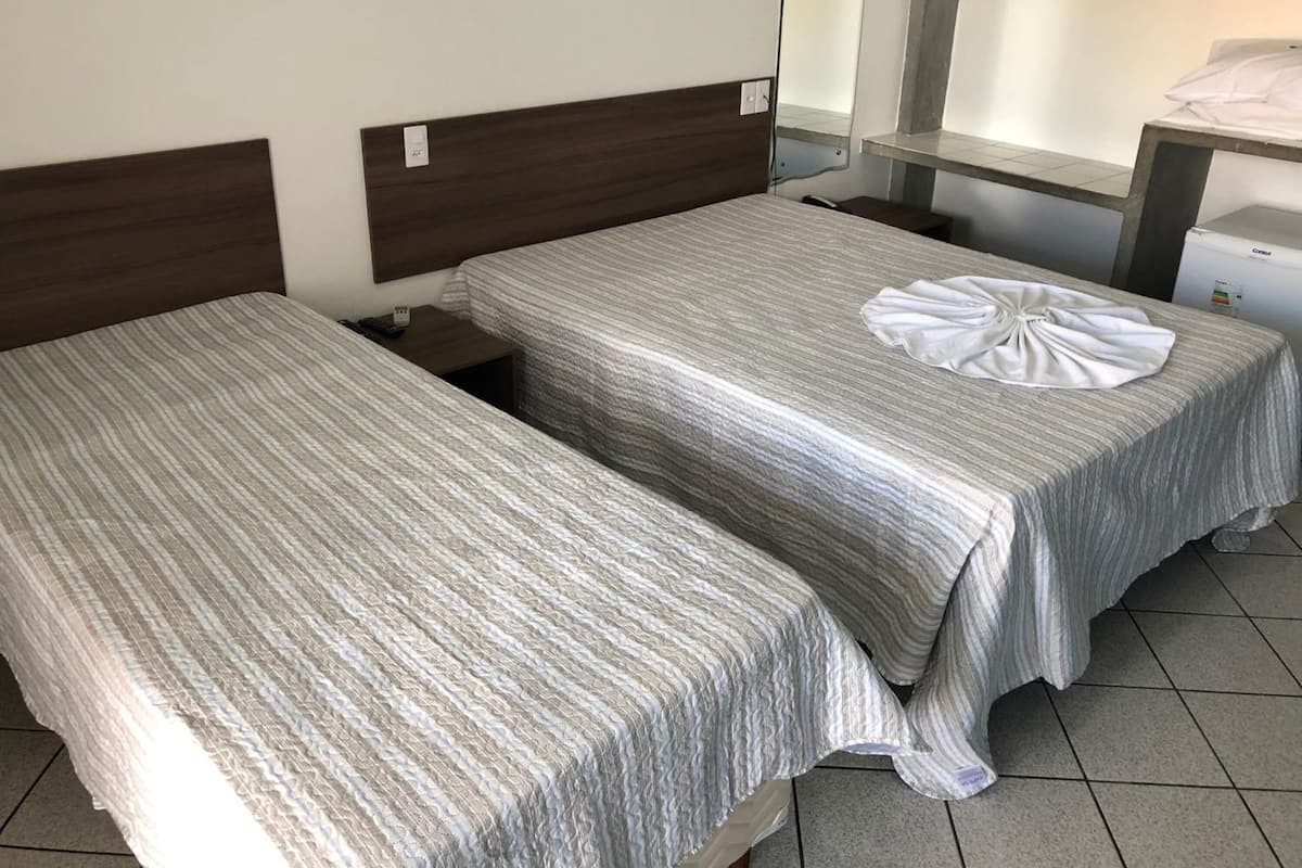 A hotel room with two single beds, a bedside table with a phone, a mirror, and a small desk with a lamp.