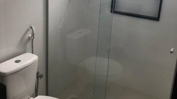 Een badkamer met een douche met glazen wand, toilet en wastafel.