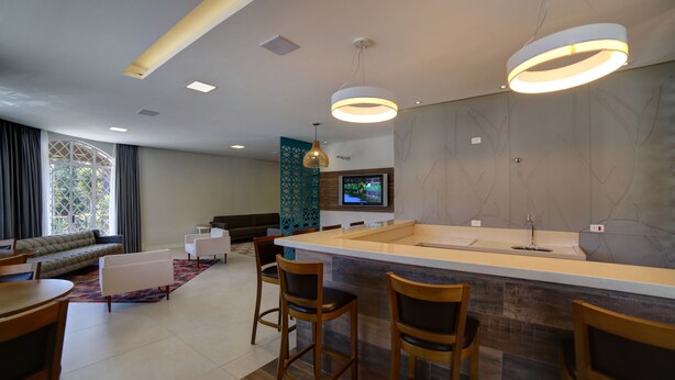 A modern kitchen with a bar area, a dining table with chairs, a sofa, and a TV mounted on the wall. - Moinho Itália Hotel (Campos do Jordão)